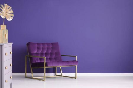宽阔的扶手椅, 抽屉的胸和金色的装饰品设置在客厅内部的紫色, 空墙.